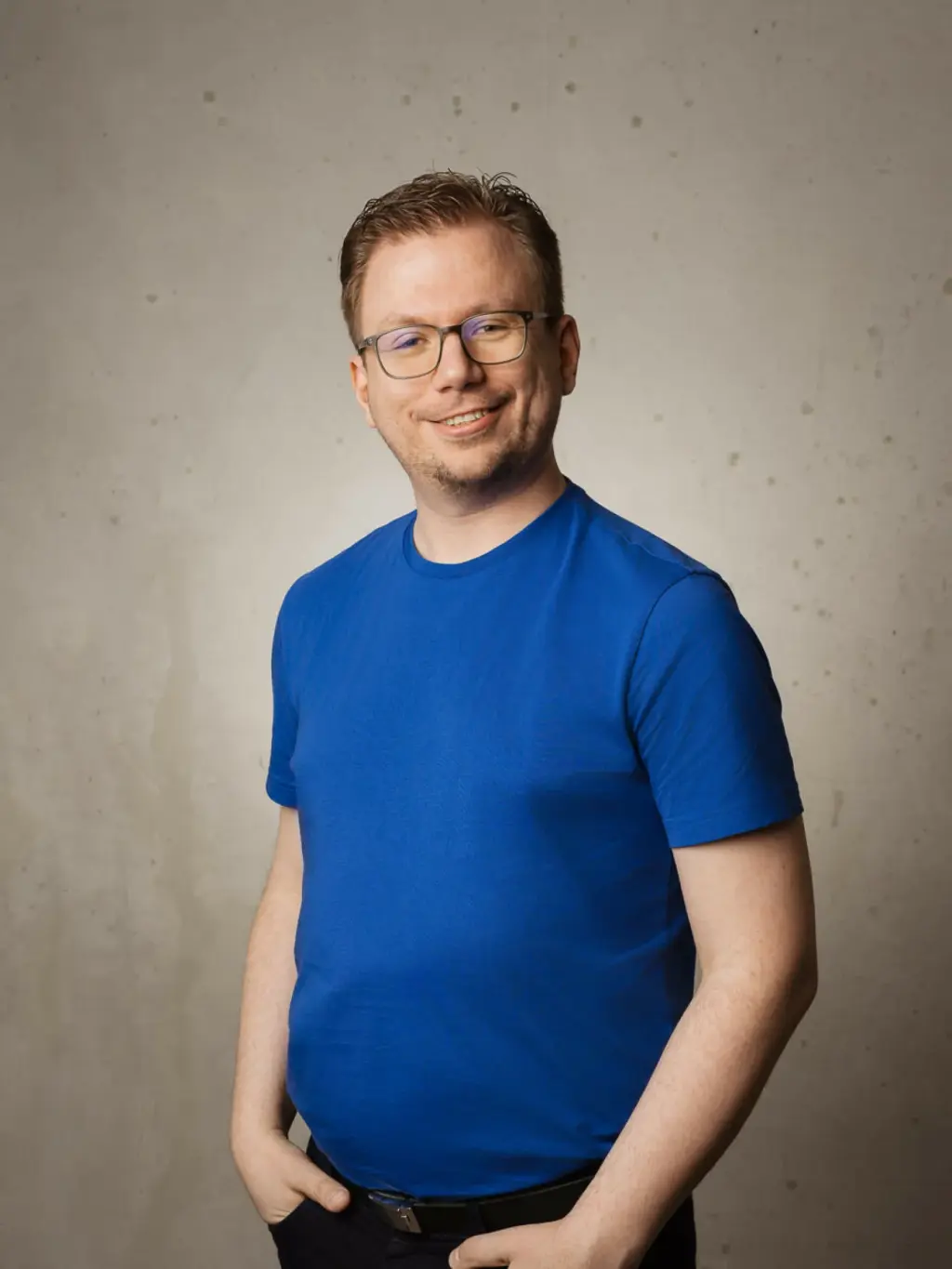 Philipp hat kurze Haare und trägt eine Brille. Er trägt ein blaues T-Shirt und schwarze Hose. Er lächelt in die Kamera.